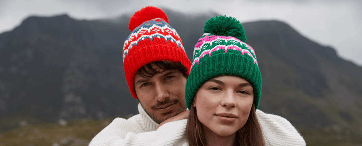 koppel poseert voor bergen met allebei een kleurrijke muts op het hoofd