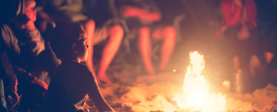een groep van een jeugdbeweging zit 's avonds gezellig rond een kampvuur