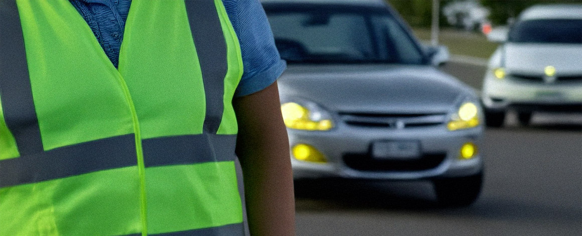 geel fluohesje op voorgrond met op achtergrond enkele auto's op een straat