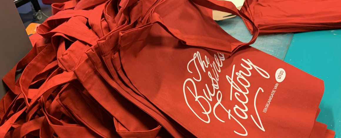 rode totebags met bedrukking voor Unizo die klaar liggen om uitgedeeld te worden op een beurs