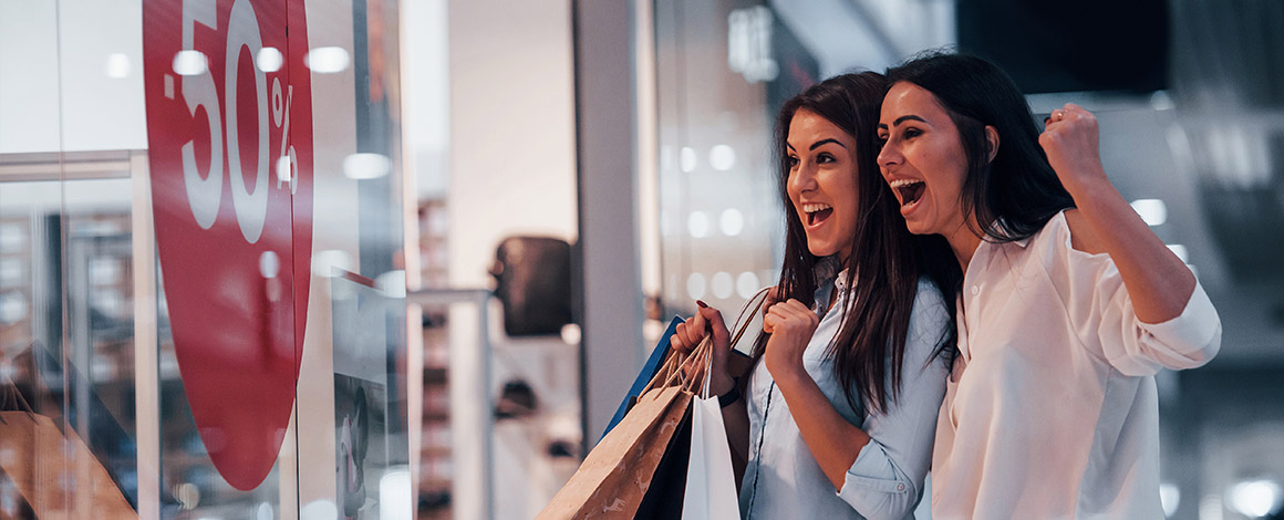 2 shoppende dames staan voor een etalage met een grote raamsticker die 50% korting aankondigt