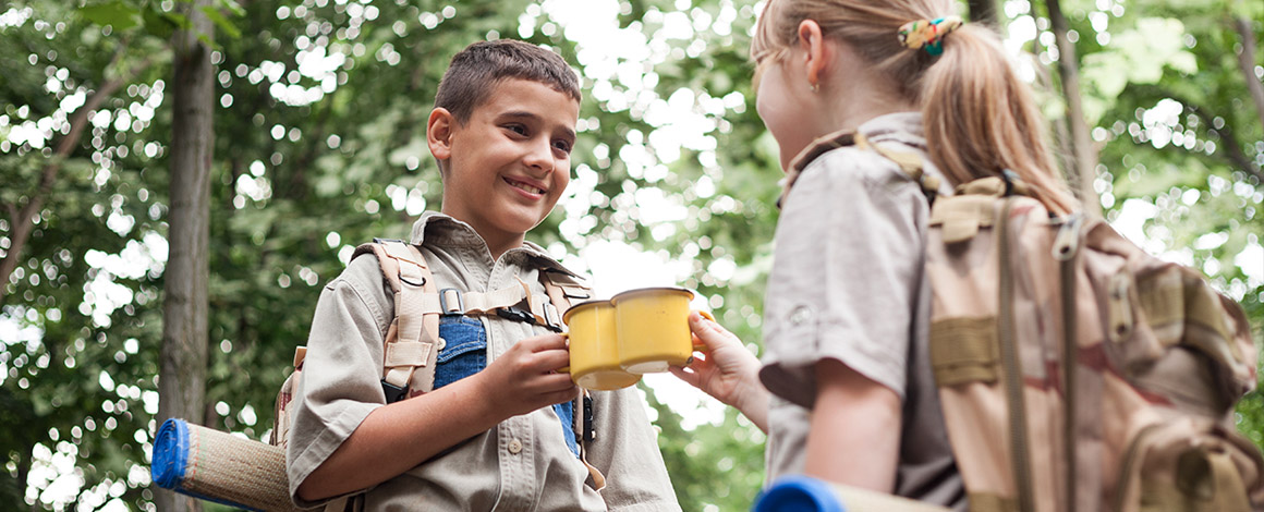 2 scouts kinderen met bedrukte rugzakken en bedrukte mokken in het bos