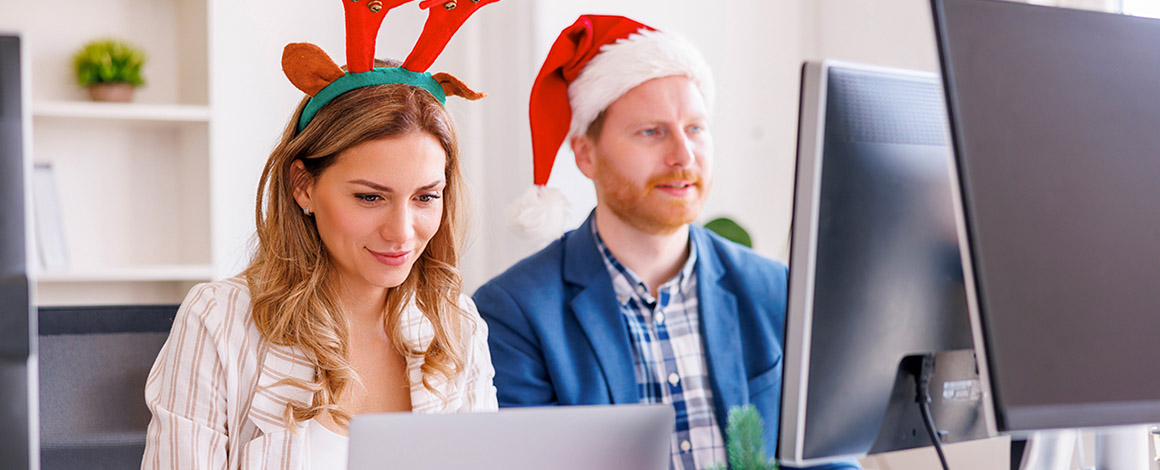 mannelijke en vrouwelijke collega zitten aan hun bureau te werken met kerstmutsen op