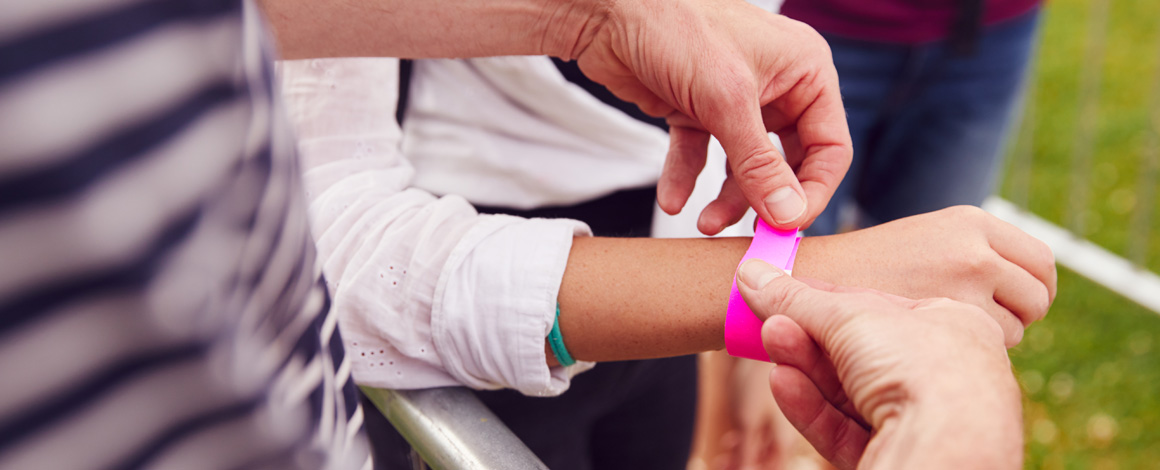 iemand brengt een roze tyvek polsbandjes aan bij een bezoeker van een outdoor event