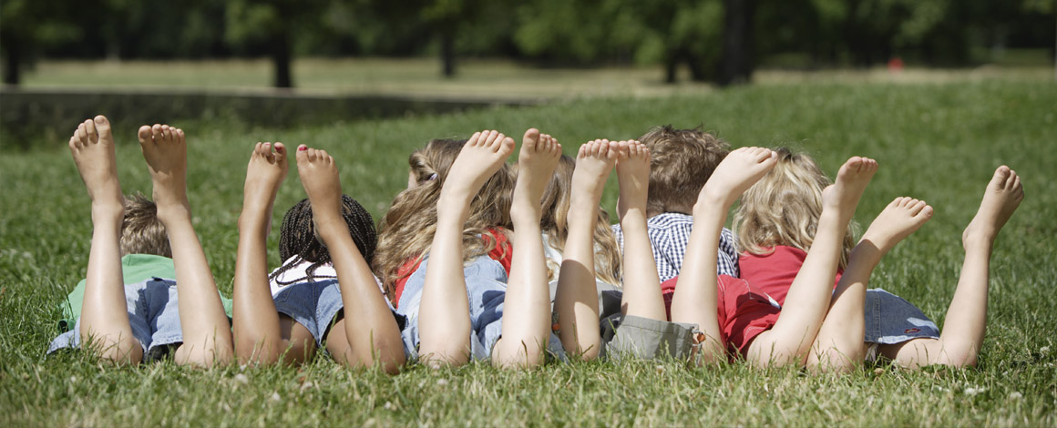 een groep kinderen ligt in het gras op een jeugdkamp met de beentjes omhoog